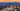 A scenic photograph of Asheville, NC from above with the blue ridge mountains and a colorful sky at sunset behind it.
