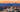 A scenic photograph of Asheville, NC from above with the blue ridge mountains and a colorful sky at sunset behind it.