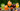 5 glasses filled with orange, green, yellow & purple iced beverages with fruit slices and herbs with trees in the background