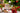 A white mug with holiday decor, sliced dried fruit, and a christmas tree around it.