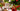 A white mug with holiday decor, sliced dried fruit, and a christmas tree around it.