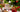 A white mug with holiday decor, sliced dried fruit, and a christmas tree around it.