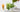Two tall glasses of iced matcha lattes sit on a light surface, one fully green and one layered with white milk and green matcha as it’s being poured. A bamboo whisk, small pitcher of milk, and a bowl of frothed matcha are arranged nearby
