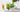 Two tall glasses of iced matcha lattes sit on a light surface, one fully green and one layered with white milk and green matcha as it’s being poured. A bamboo whisk, small pitcher of milk, and a bowl of frothed matcha are arranged nearby
