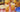 A gingham tablecloth with fried chicken, pasta salad, fruit, plates, and two glasses of iced tea with lemon wedges.