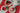 set of 3 white tea plates with strawberry desserts with a white pitcher on a red place mat