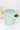 Mint green mug with a lid on a white surface with flowers in the background