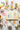 A styled tea-themed flat lay featuring colorful teacup-shaped bookmark tags attached to an open vintage book, surrounded by teacups, teapots, flowers, and tea on a light fabric surface.