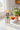 Clear water bottle with floral and insect design on a kitchen counter with fruits and a plant.