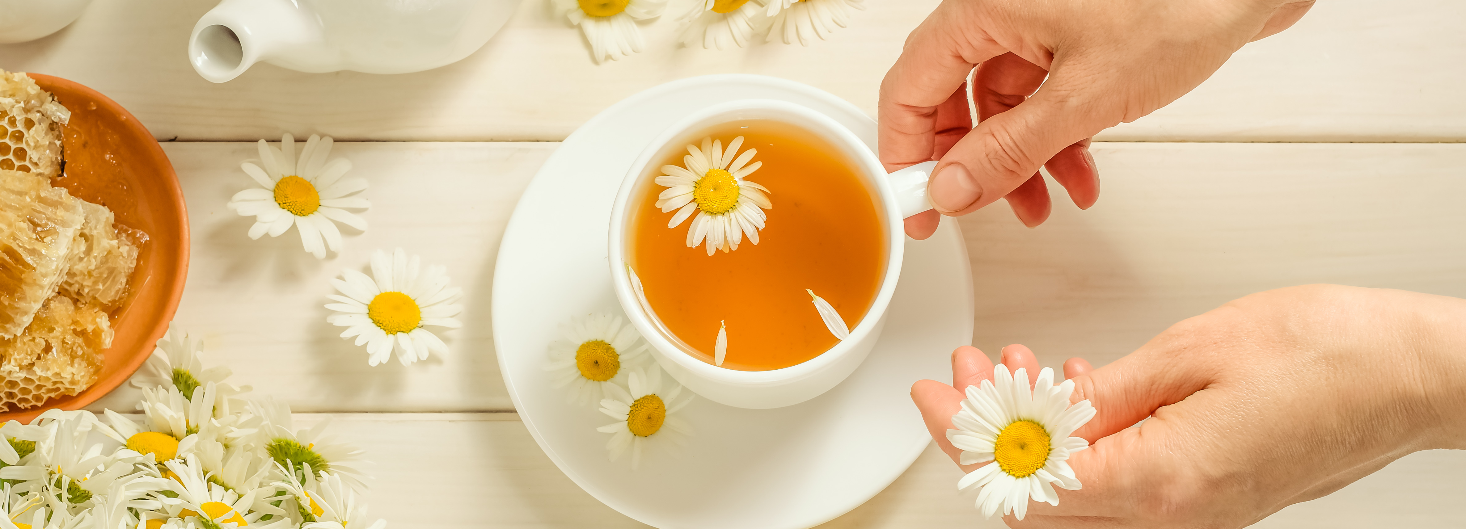 Tea cup with flowers on a wooden table, surrounded by tea leaves and flowers.