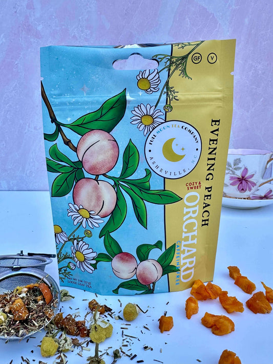 A pouch of Evening Peach Orchard caffeine free tea with tea spilling out of a tea infuser, dried peaches, and chamomile around it.