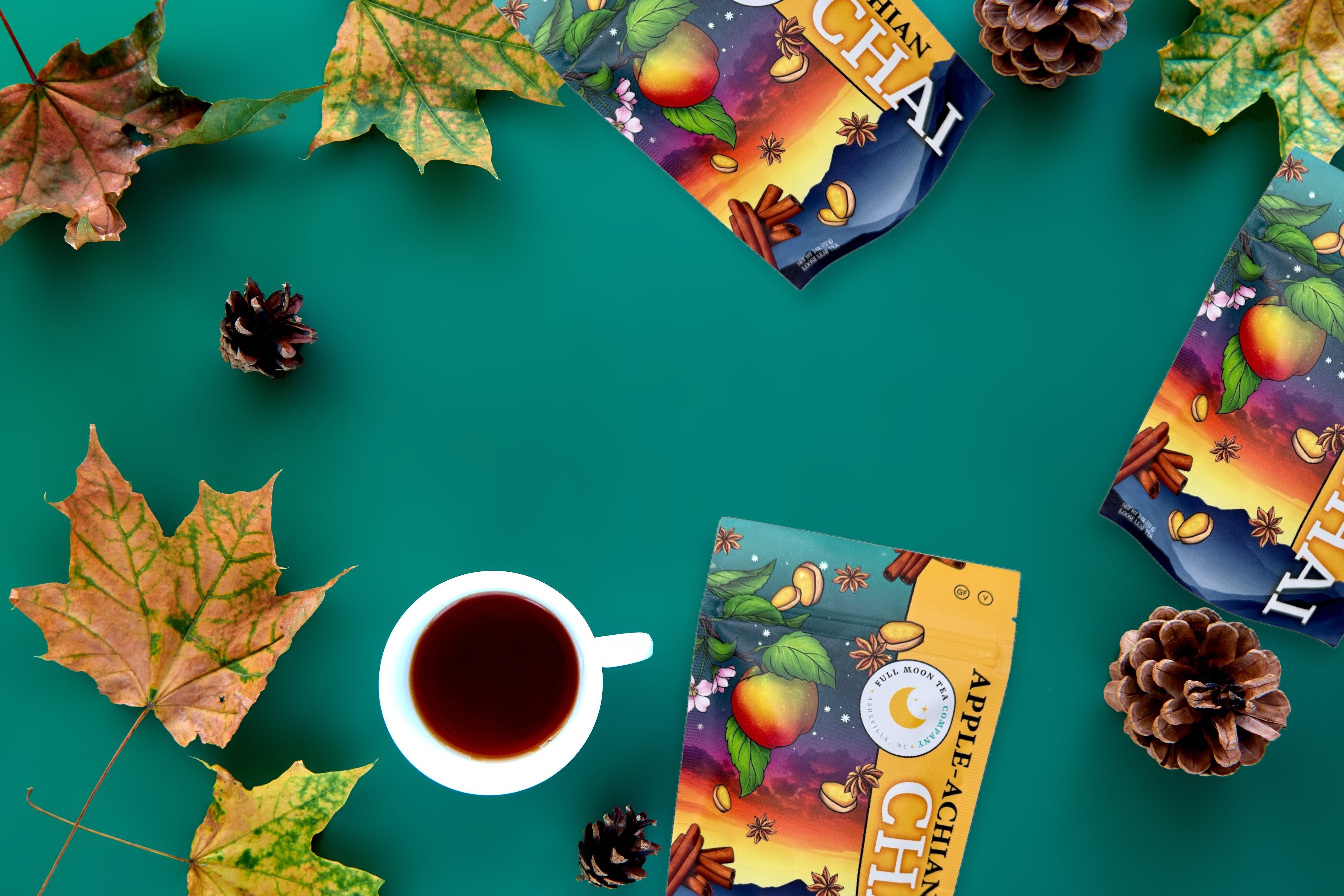 Tea bags with colorful packaging, a cup of tea, and autumn leaves on a teal background